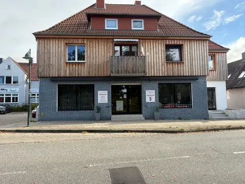 Zweigeschossiges Geschäftshaus mit blauer Klinkerfassade, großen Schaufenstern, Holzverkleidung im Obergeschoss und rotem Ziegeldach an einer Straße