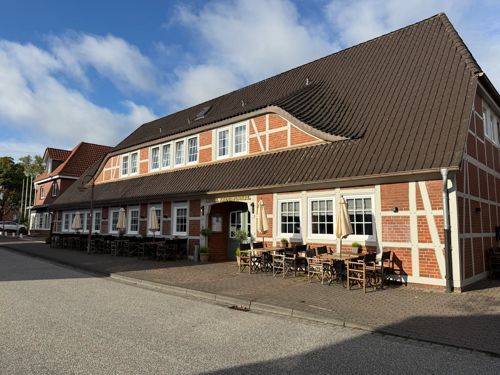 Fachwerkgebäude des Hotels Krohwinkel mit großem Ziegeldach und Außenterrasse an einer Straße bei Sonnenschein