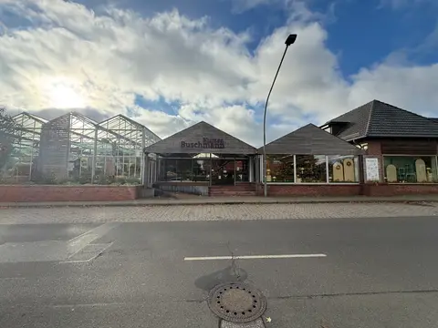 Eingang des Blumengeschäfts Blumen Buschmann mit Holzgiebel, Glasgewächshäusern links und Schaufenstern rechts an einer Straße