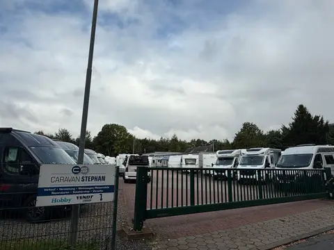 Gelände eines Caravanhändlers mit Wohnwagen und Wohnmobilen hinter grünem Schiebetor, vorne das Firmenschild Caravan Stephan