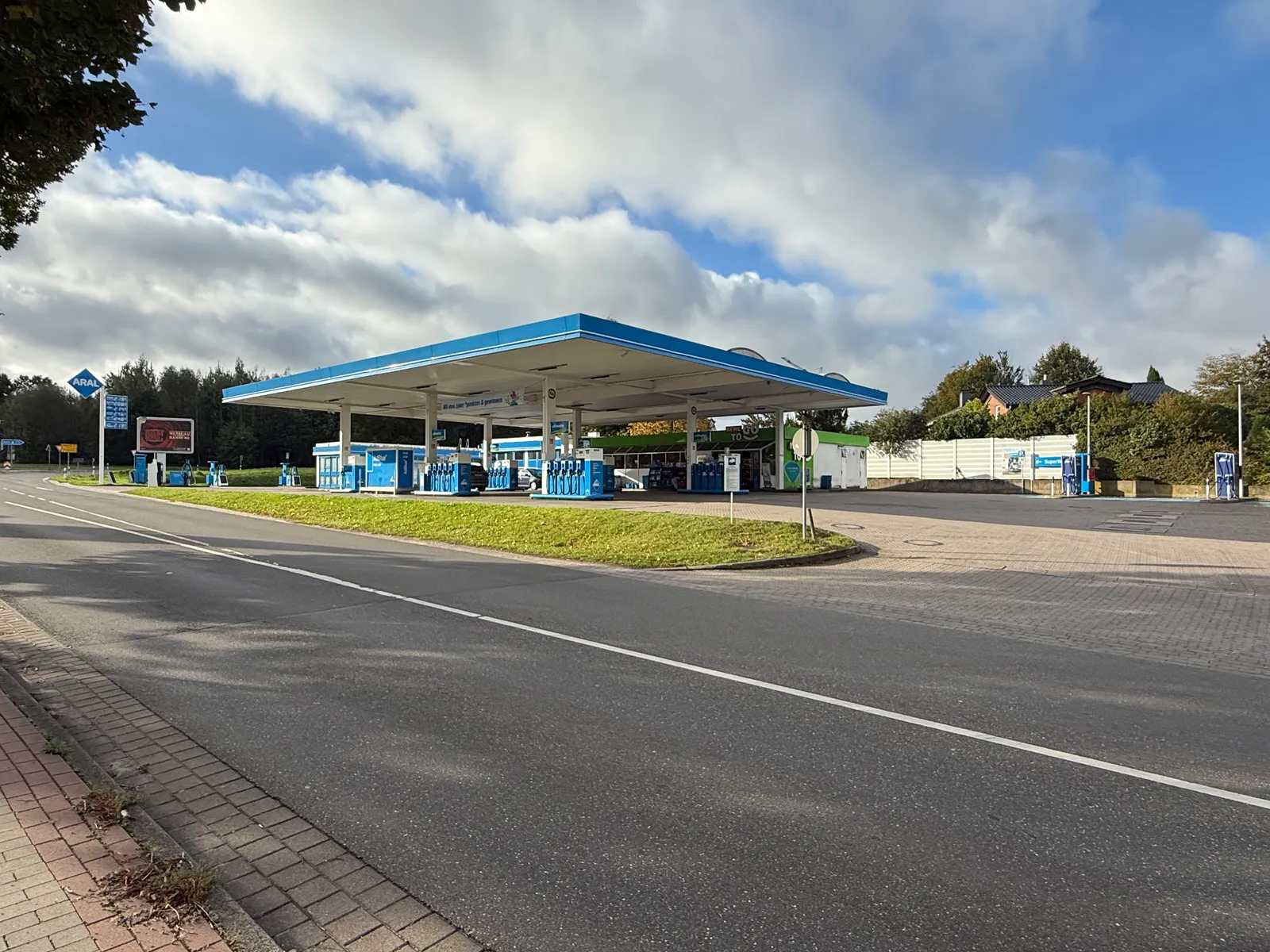 Aral-Tankstelle mit großem blau-weißem Tankdach, Zapfsäulen, Preismast und Shop an einer Straße mit Grünstreifen