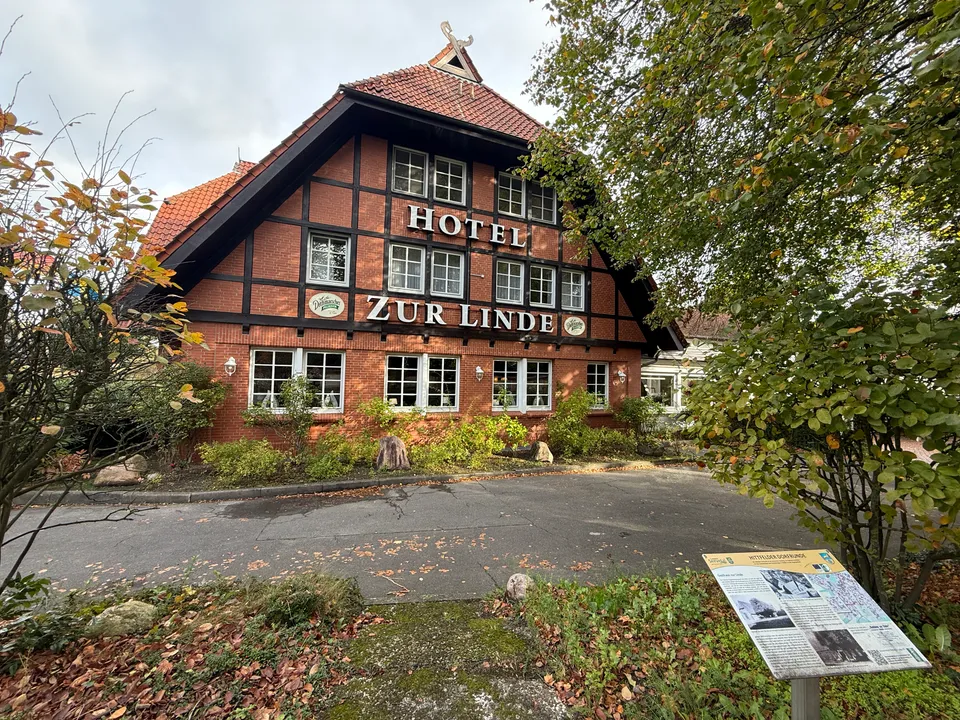 Fachwerkgiebel mit Schriftzug Hotel Zur Linde, davor Infotafel der Hittfelder Dorfrunde und Herbstlaub