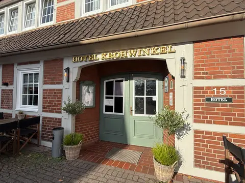 Eingang des Hotels Krohwinkel mit grüner Holztür, goldenem Schriftzug, Fachwerkfassade und Olivenbäumchen in Körben