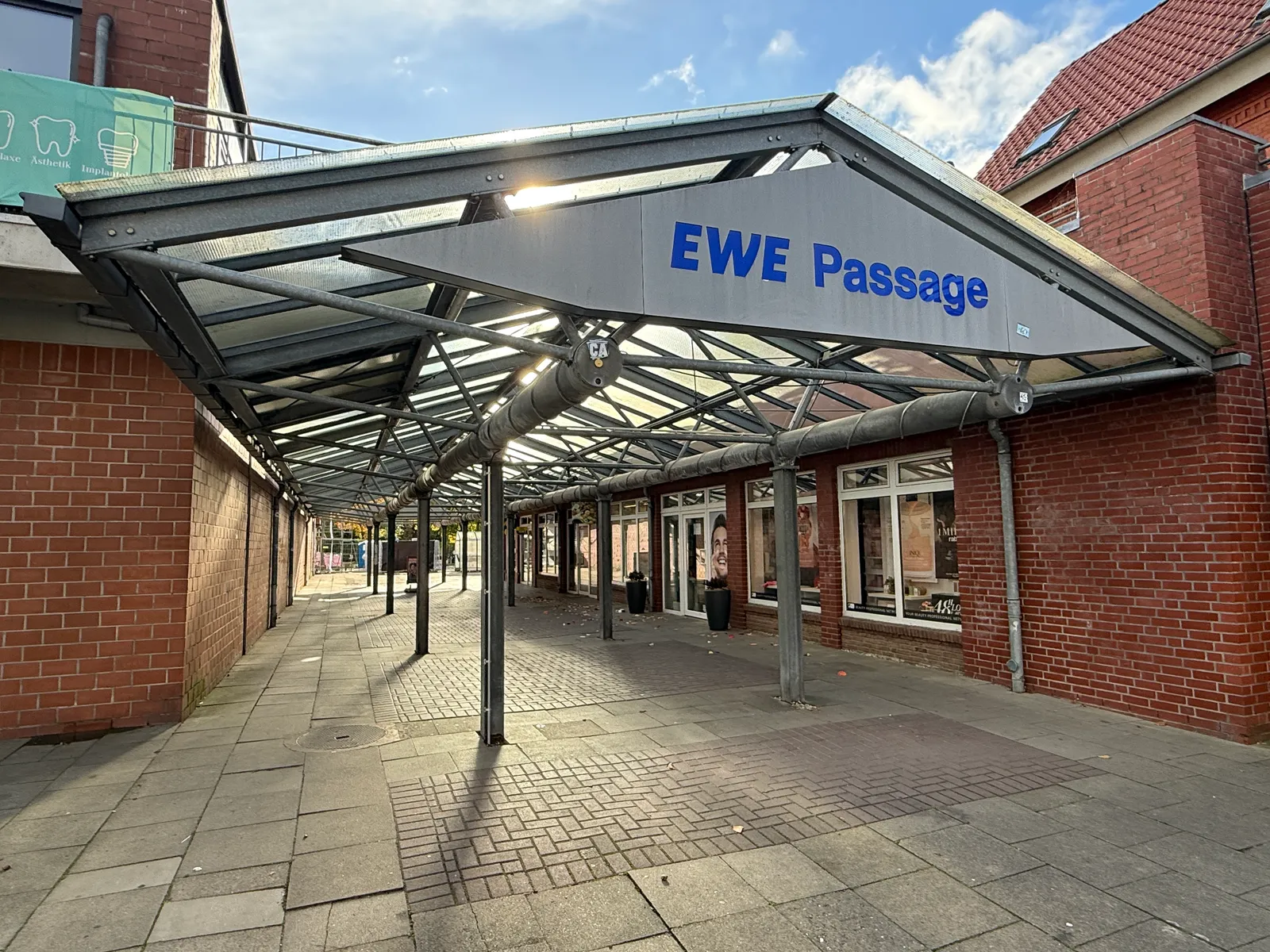 Eingang der EWE Passage mit Glas-Stahl-Vordach, Backsteinfassaden, Ladenfronten und gepflastertem Gang bei Sonnenschein