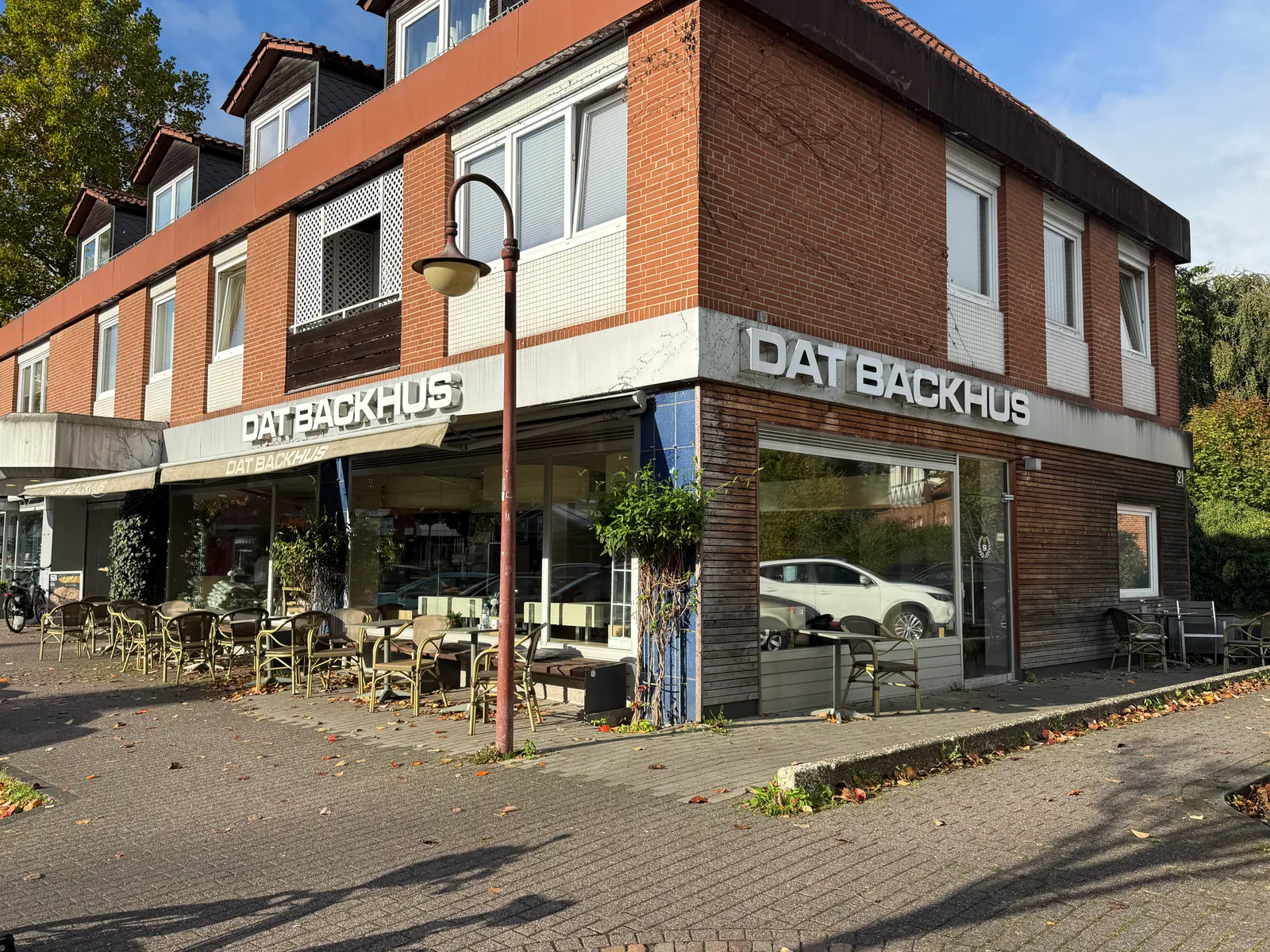 Eckgebäude aus rotem Klinker mit Bäckerei-Café „Dat Backhus“, Außenbestuhlung auf gepflastertem Gehweg und Straßenlaterne