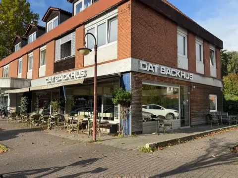 Eckgebäude aus rotem Klinker mit Bäckerei-Café „Dat Backhus“, Außenbestuhlung auf gepflastertem Gehweg und Straßenlaterne