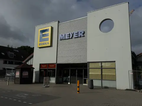 Supermarktfassade mit EDEKA-Logo, Schriftzug MEYER, rundem Wandausschnitt, Eingangsbereich und Bäckerei KNAACK unter bewölktem Himmel