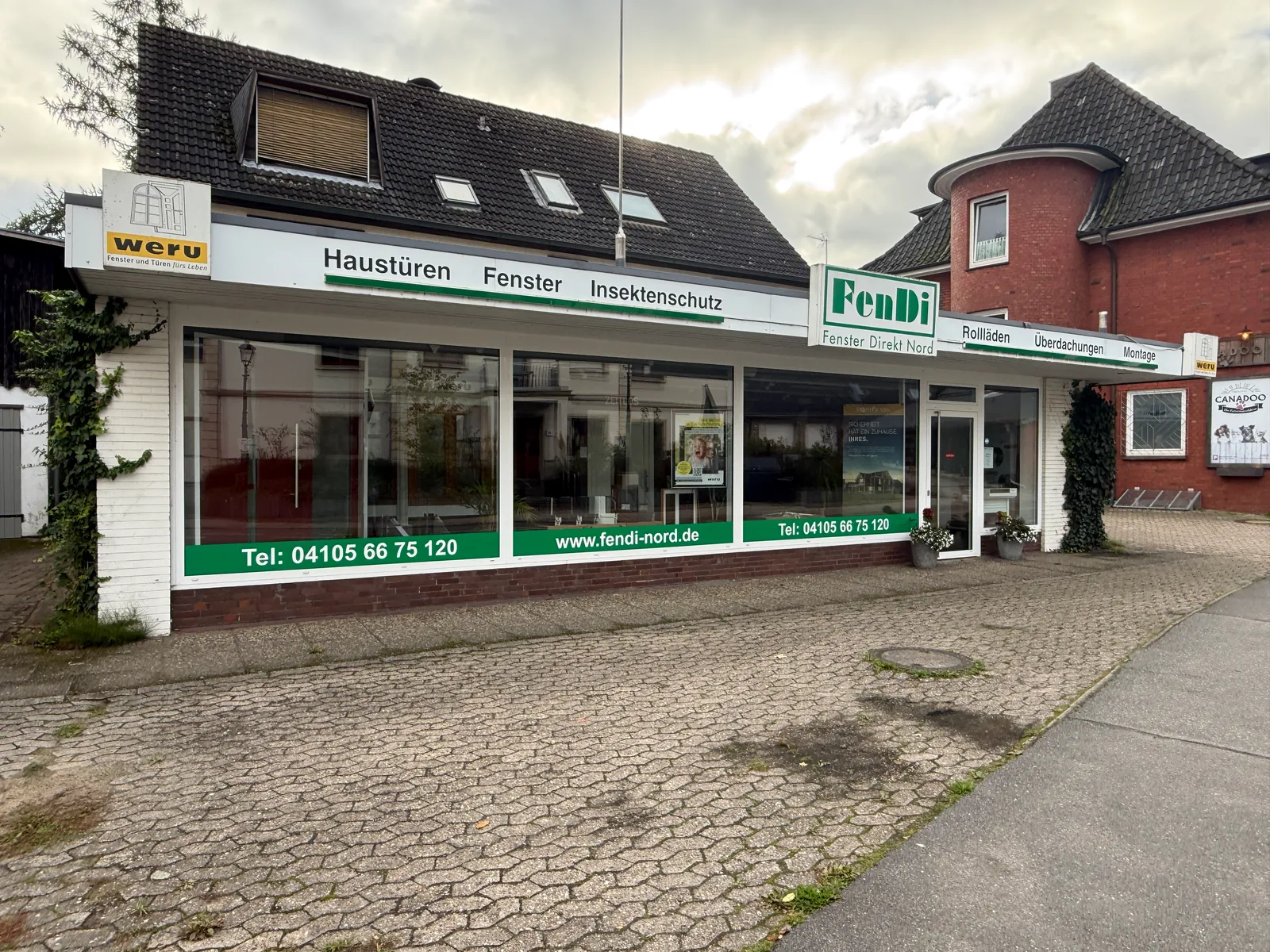 Ladenfront von FenDi Fenster Direkt Nord mit großen Schaufenstern, grünen Werbeschriftzügen und gepflastertem Vorplatz