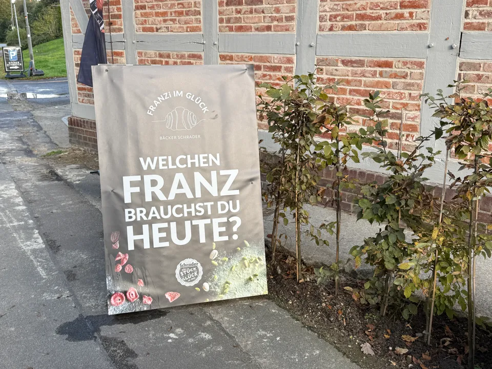 Werbeaufsteller mit dem Text „Welchen Franz brauchst du heute?“ vor einer Fachwerkwand mit Ziegeln