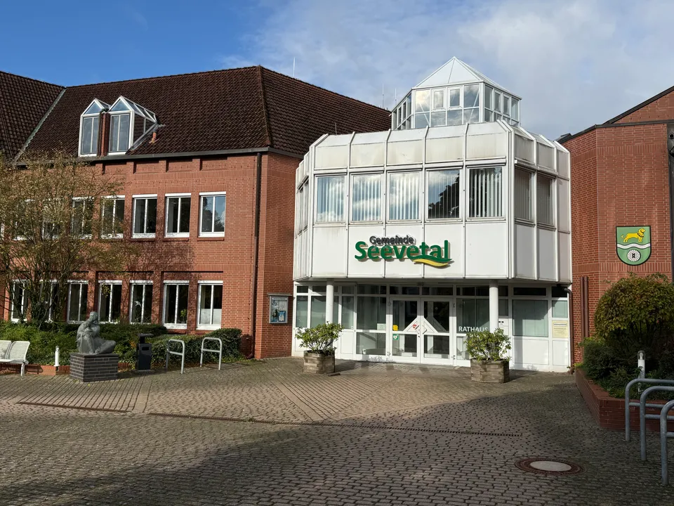 Rathaus Seevetal mit weißem Eingangsbau und Glasaufsatz zwischen Klinkergebäuden, davor ein gepflasterter Vorplatz