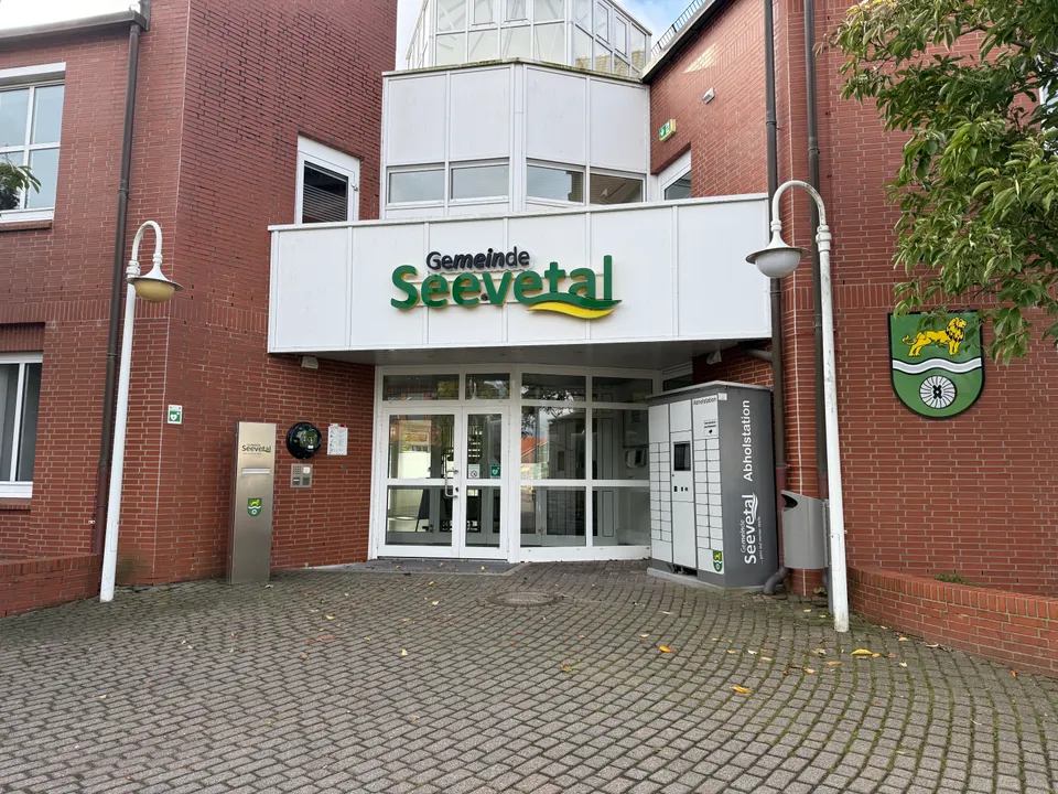 Rathauseingang mit Schriftzug Gemeinde Seevetal, Abholstation mit Schließfächern, Laternen und Gemeindewappen an einer Klinkerwand