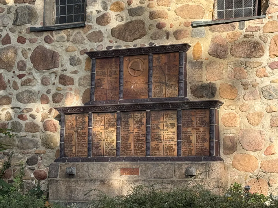 Gedenktafeln für Gefallene des Ersten Weltkriegs mit Stahlhelm-Relief und Namenslisten an einer Feldsteinwand