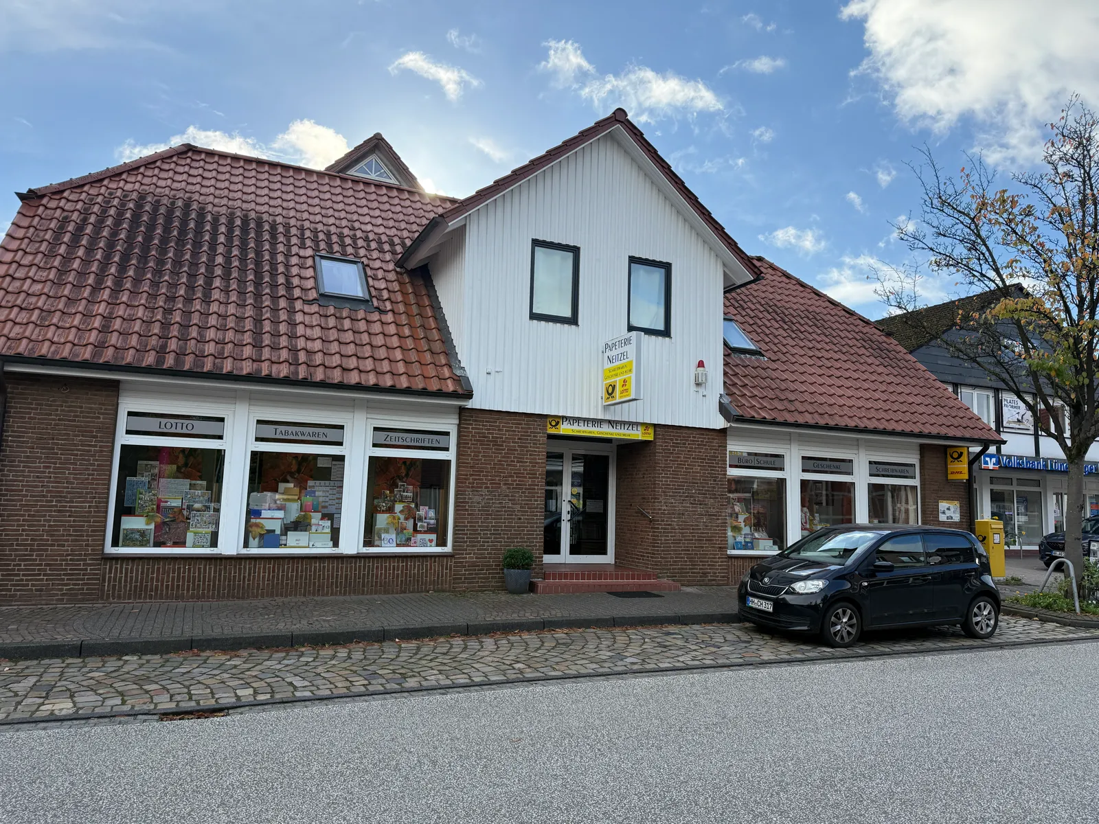 Klinkergebäude der Papeterie Neitzel mit Schaufenstern für Lotto, Tabakwaren und Zeitschriften, davor ein parkendes Auto