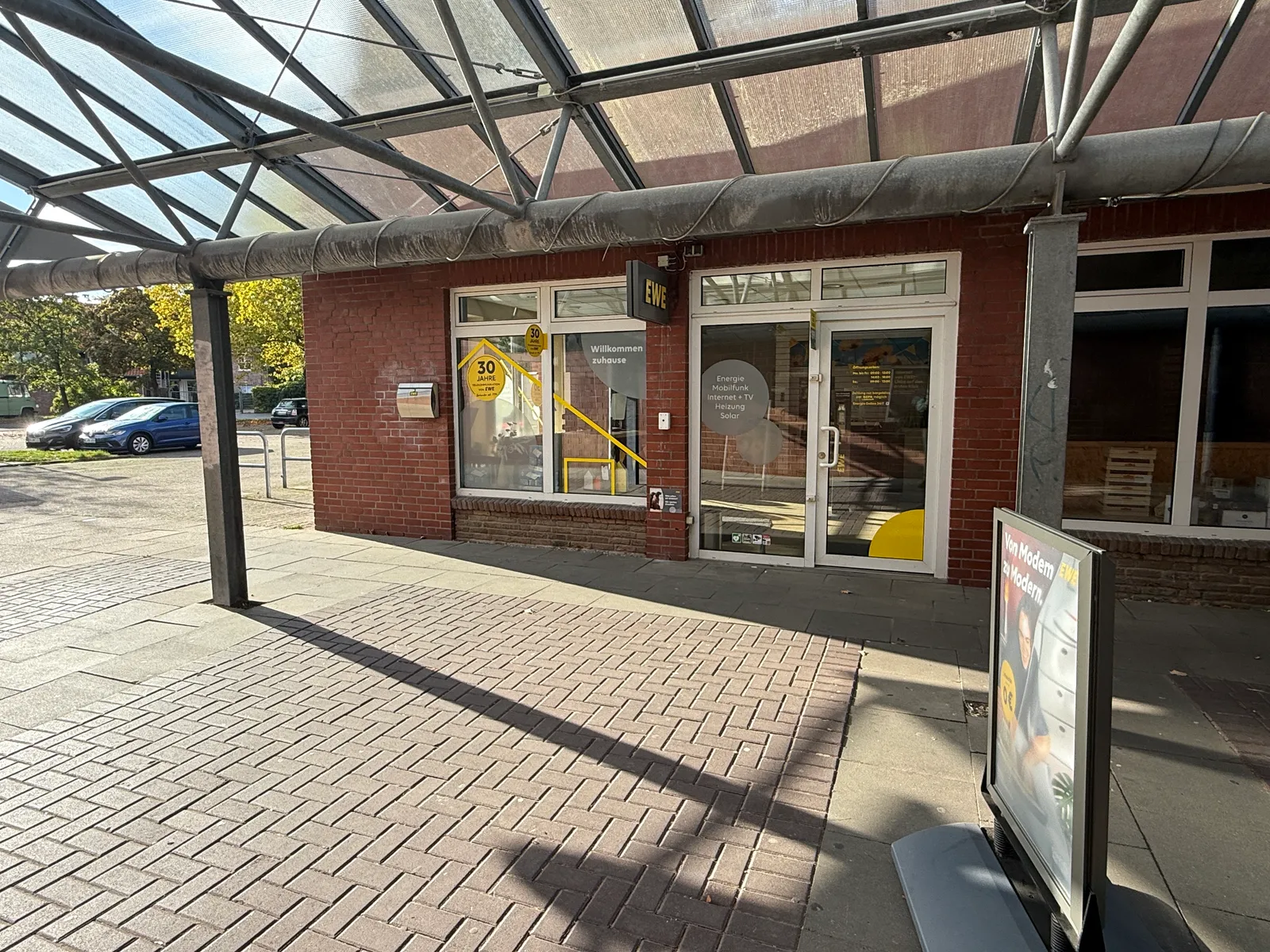 Ladeneingang des EWE-Shops in einer Klinkerpassage mit Glasdach, gelb beklebten Schaufenstern und Werbeaufsteller davor