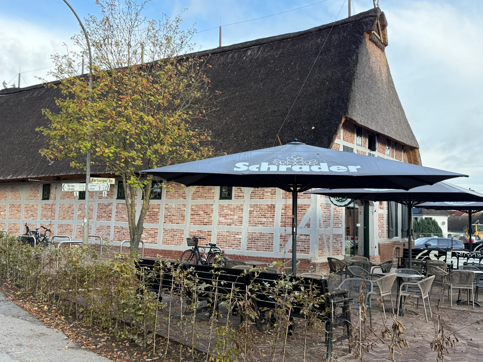 Reetgedecktes Fachwerkhaus mit Außenterrasse, Sonnenschirmen mit Schrader-Aufdruck, Stühlen und abgestellten Fahrrädern