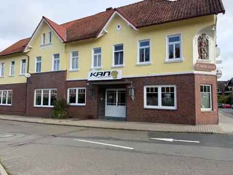 Gelb-rotes Eckgebäude mit Klinkersockel, Schild „KAN Kampfsport Akademie Nord“ über weißer Eingangstür und Figur an der Hausecke