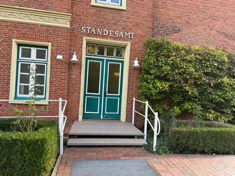 Grüne Doppeltür mit Inschrift Standesamt in roter Backsteinfassade, davor Steinstufen mit weißen Handläufen und Buchsbaumhecken